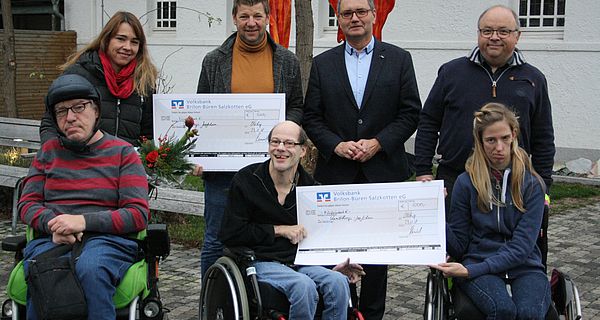 Dr. Andreas Perniok und Walter Hoffmann (hinten rechts) überreichen die symbolischen Schecks an Kunsttherapeutin Melanie Vogel und Mobilitätscoach Jürgen Mies (hinten links) und an Teilnehmer der beiden Angebote.